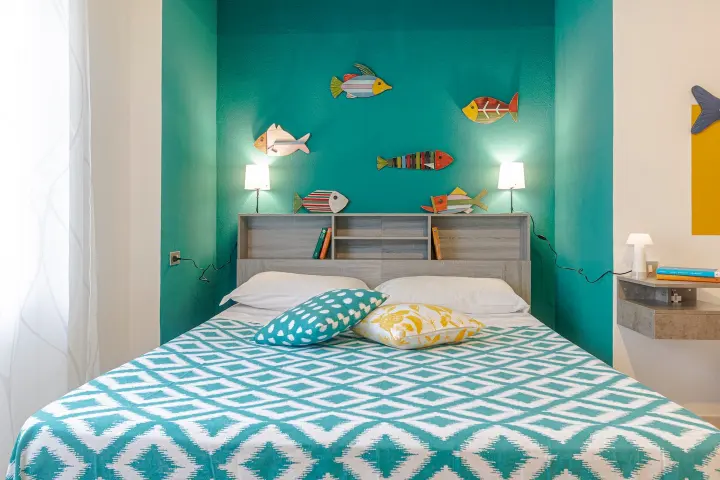 Letto matrimoniale con copriletto turchese e pesci decorativi colorati sulla parete.