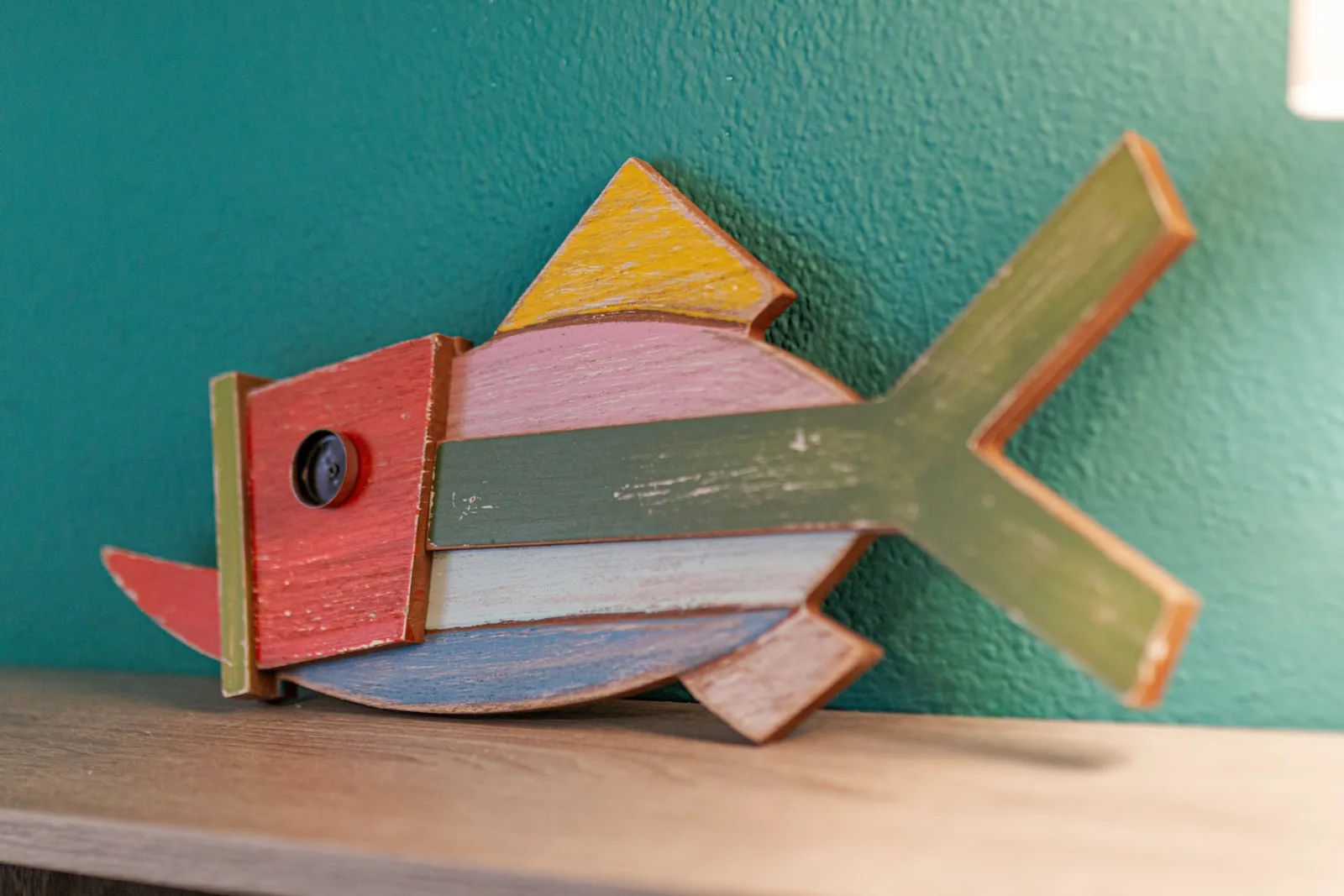 Pesce decorativo in legno colorato sulla parete turchese della camera.
